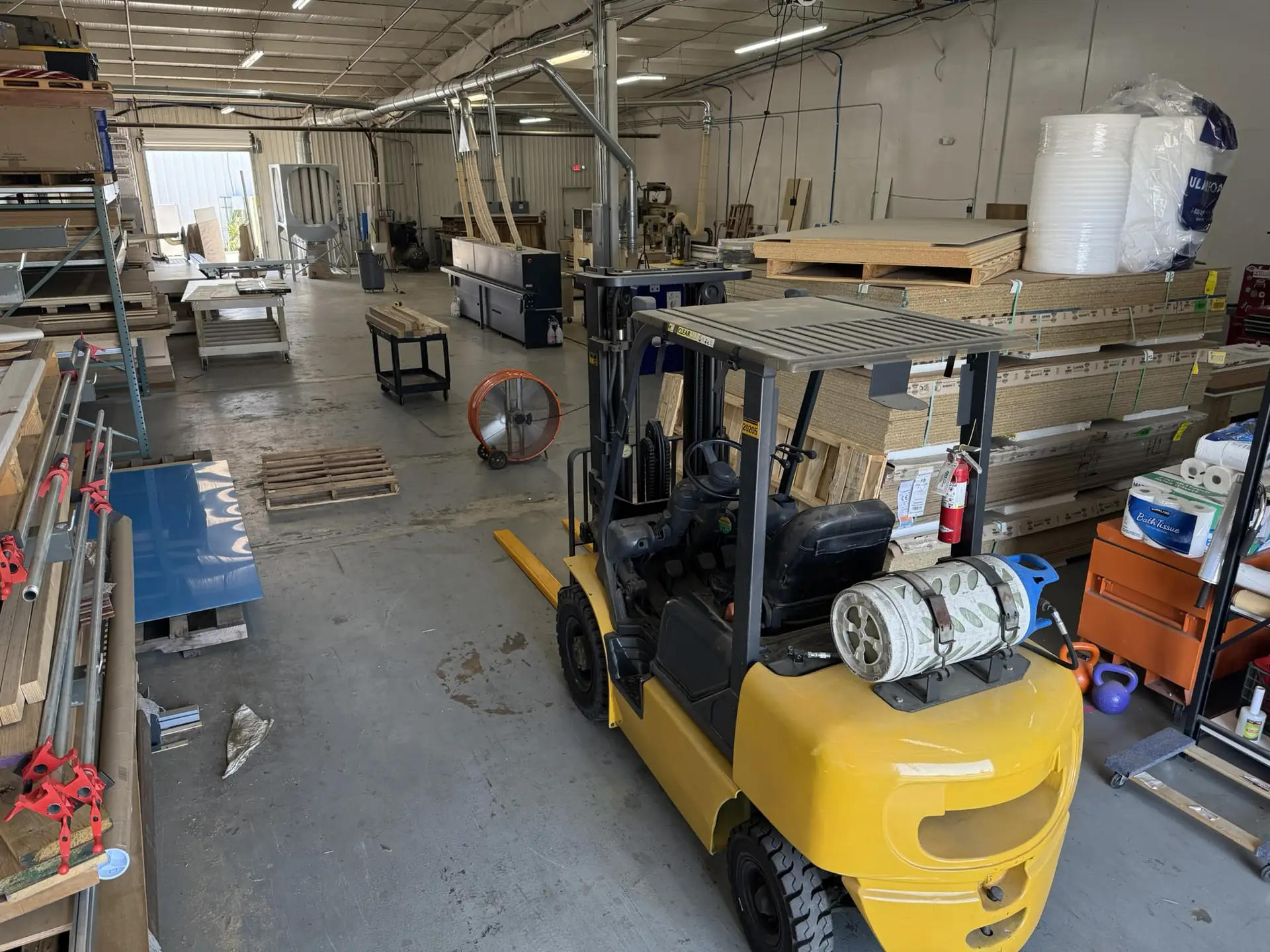 A forklift moving material down the aisle between the lumber racks and the work tables