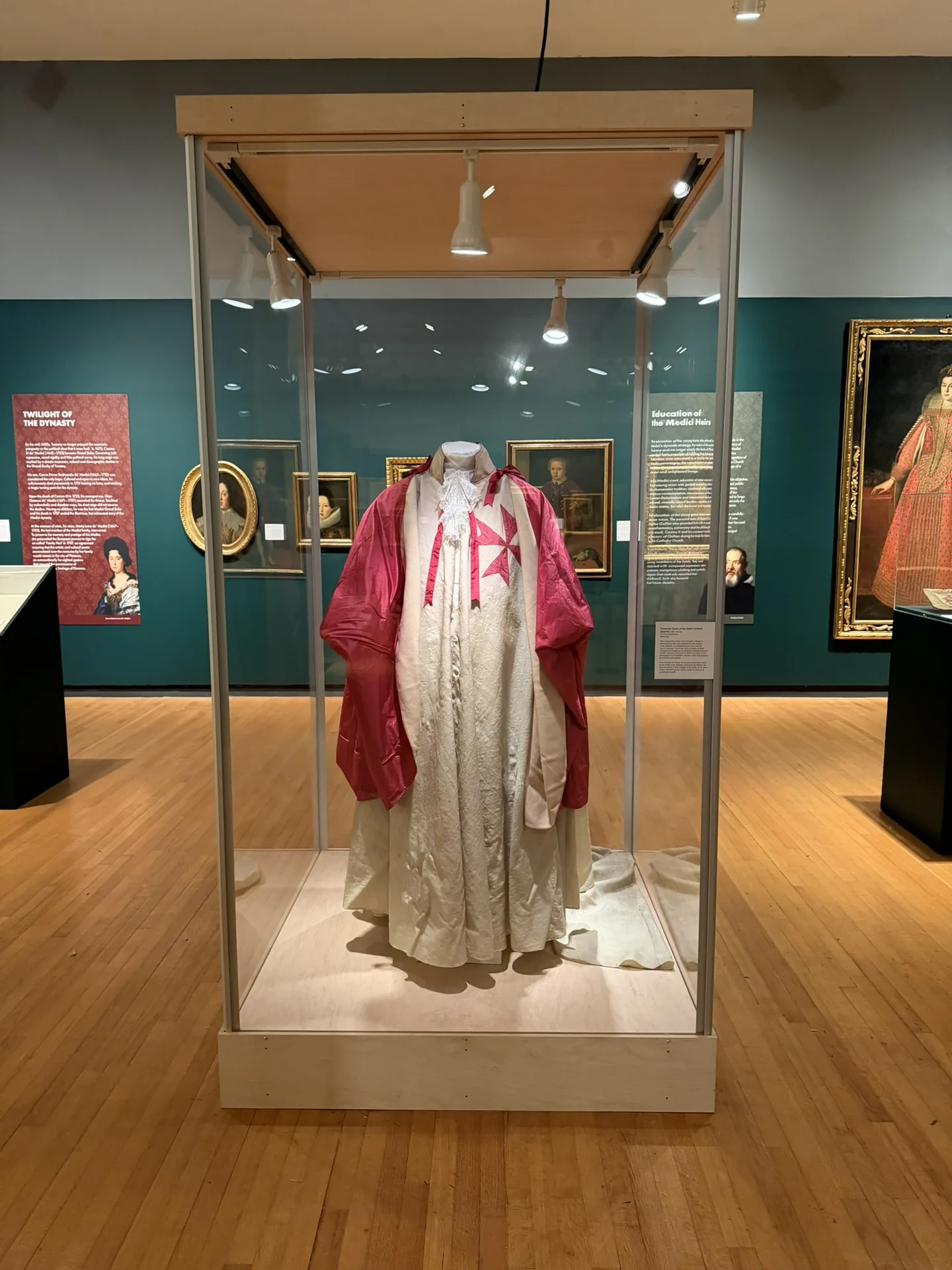 A full-height glass vitrine on a maple base displaying a ceremonial robe in a gallery