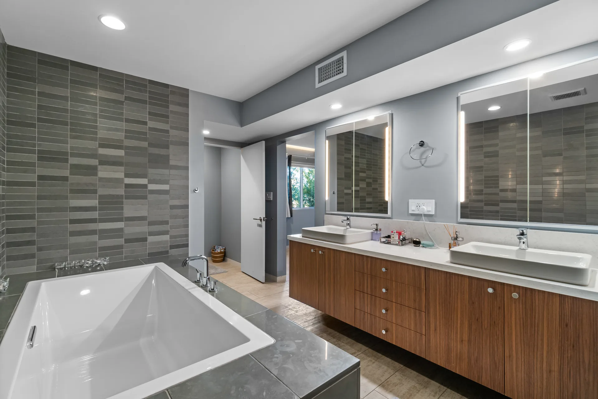 A primary bathroom with a floating walnut double vanity and lit mirrors