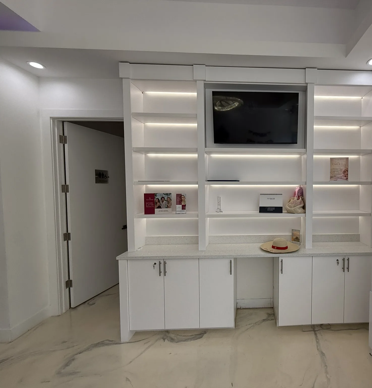 A white lacquered display wall with lit shelving and a recessed screen